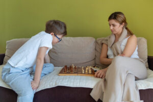 Mother And Son Focused On Chess Game. A Young Boy And His Mother Sit On A Couch, Concentrating On A Chess Match, Showing Focus And Quiet Bonding Time.